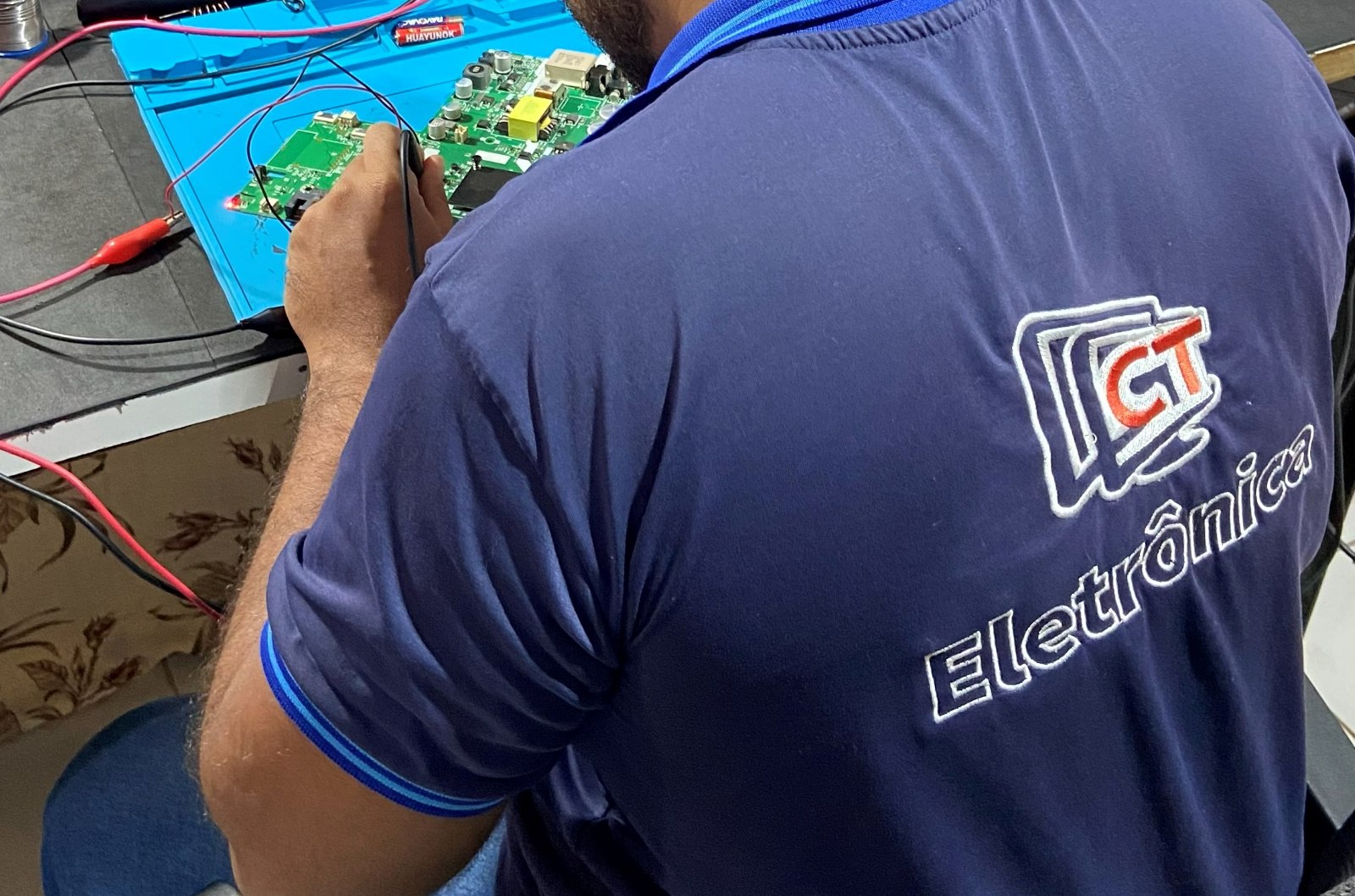 Técnico da CT Eletrônica consertando a placa de uma TV na bancada